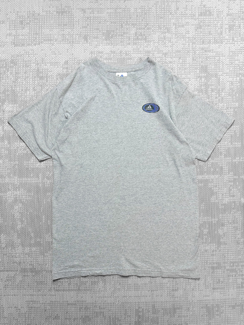 Adidas short-sleeve grey T-shirt with front logo badge featuring text, stripes, and a blue basketball graphic; back has bold basketball-themed design.